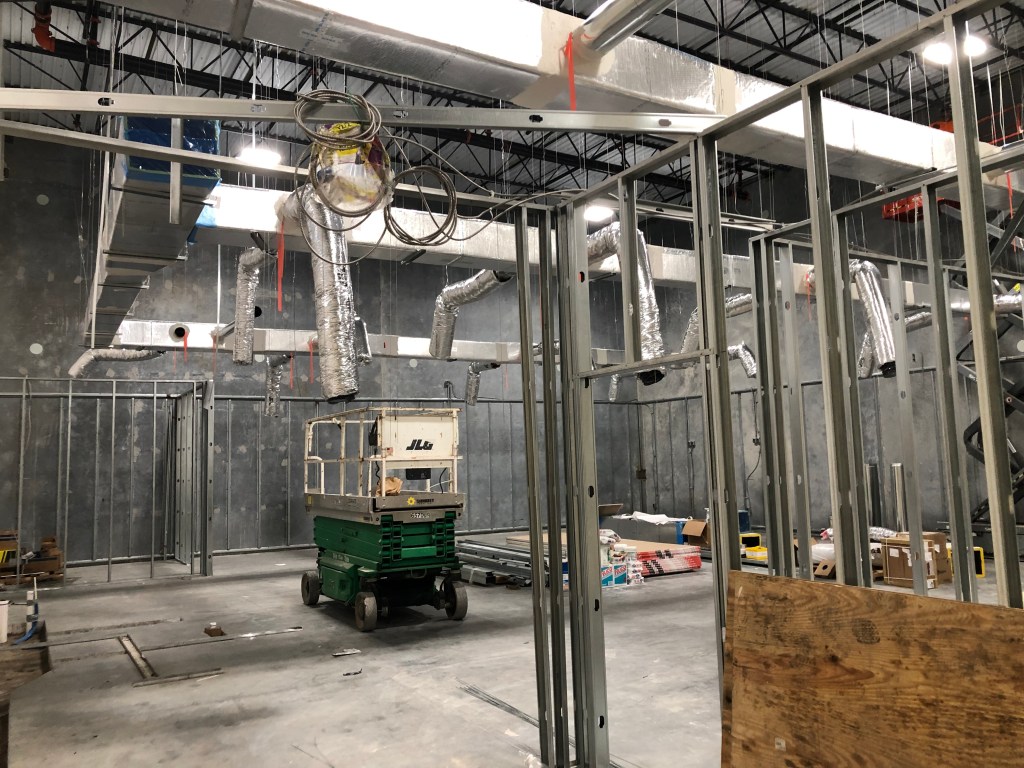 Interior view of a commercial construction site featuring metal framework, ductwork, and construction equipment.