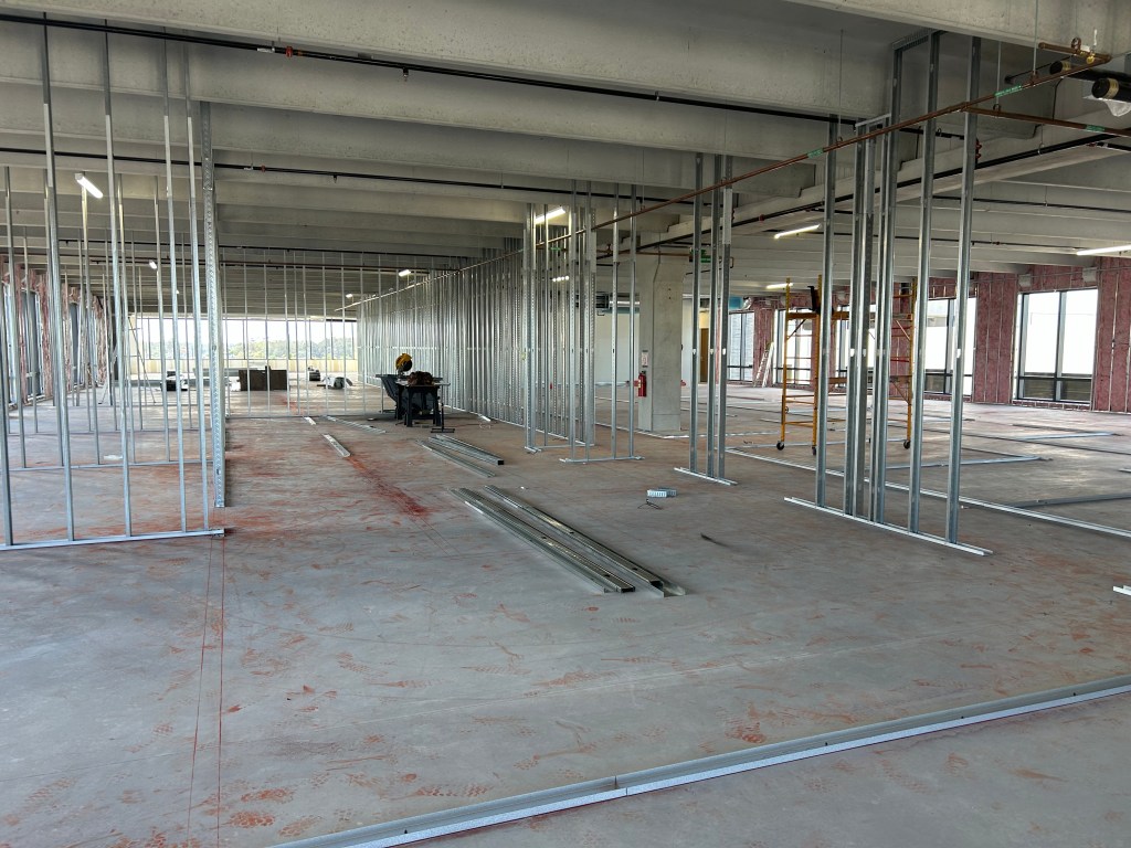 Interior view of an under-construction office space showing metal framing, unfinished floors, and tools.