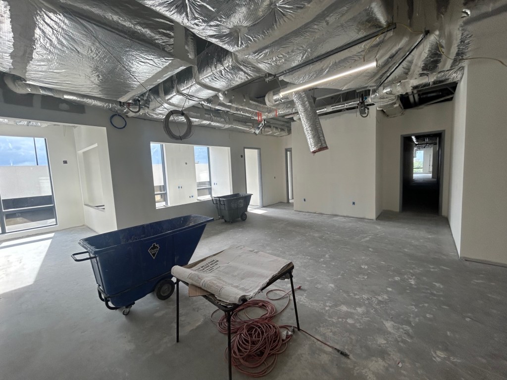 Interior view of a partially constructed office space with exposed ceilings, construction materials, and a cart.